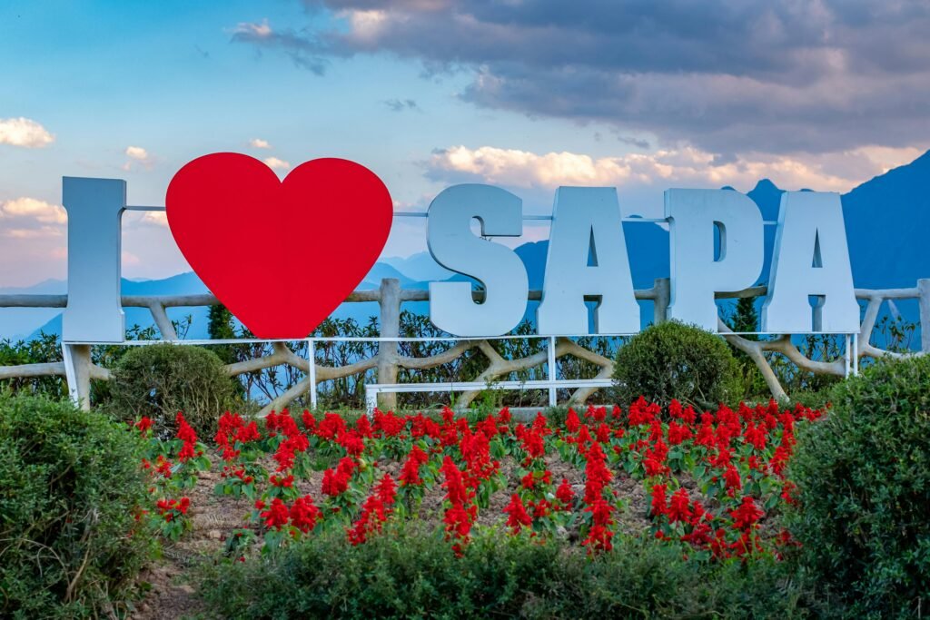 I Love Sapa sign with vibrant red flowers and scenic mountain backdrop in Vietnam.